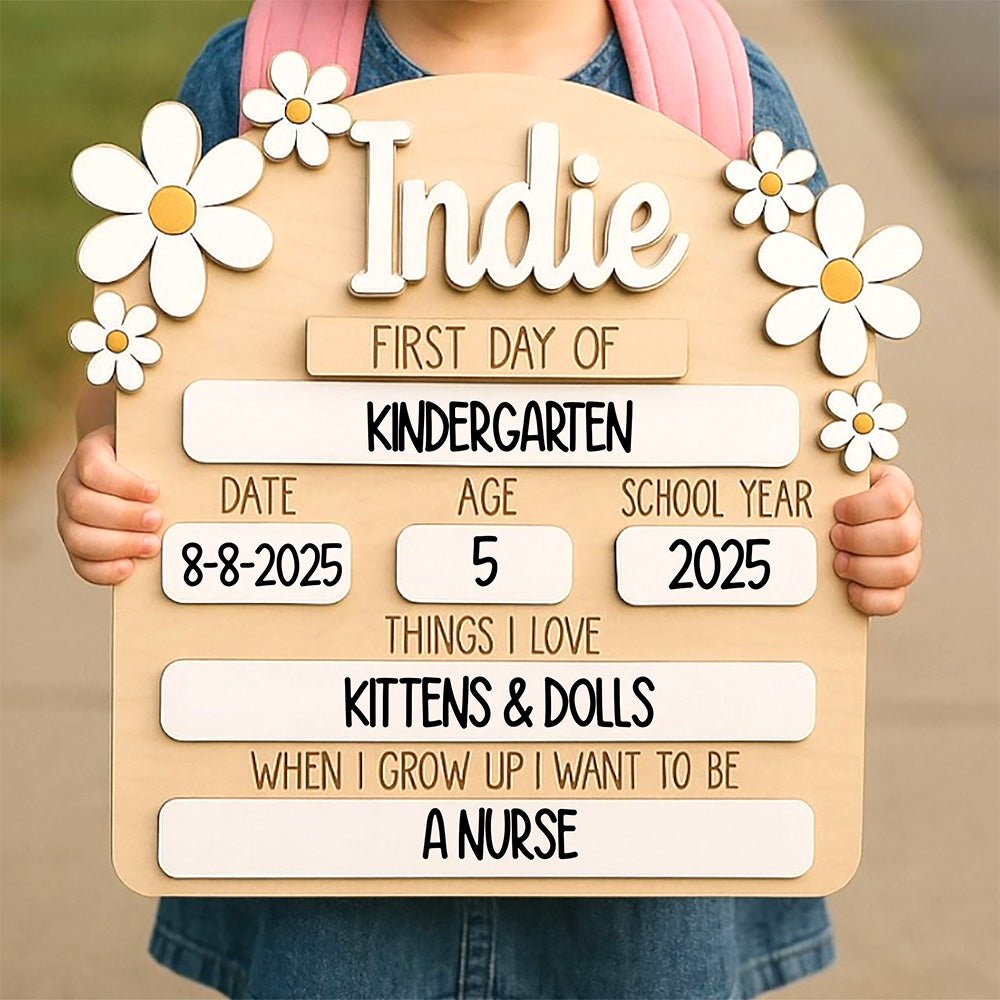 Personalized 'First Day of School' milestone board for kids, featuring a retro daisy flower design with custom name 'Indie', sections for date, age, and school year, and 'Things I Love' personalized details like 'Kittens & Dolls'.