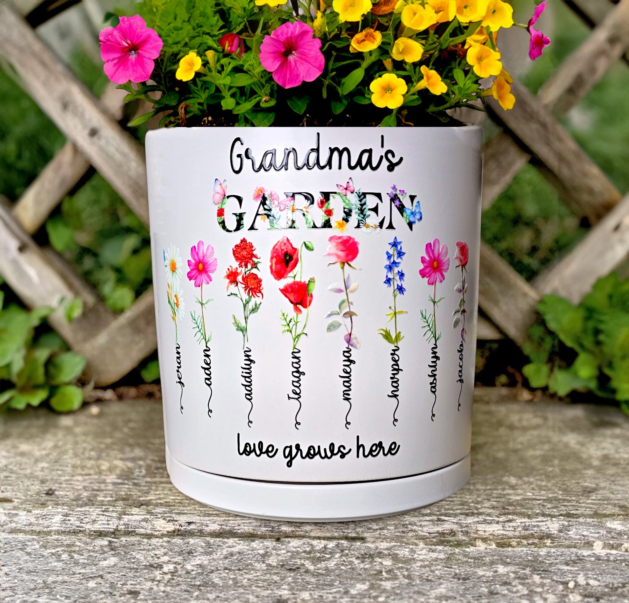 Personalized Grandma's Garden white ceramic planter pot with watercolor birth flowers and the text 'love grows here' on a rustic wood surface.