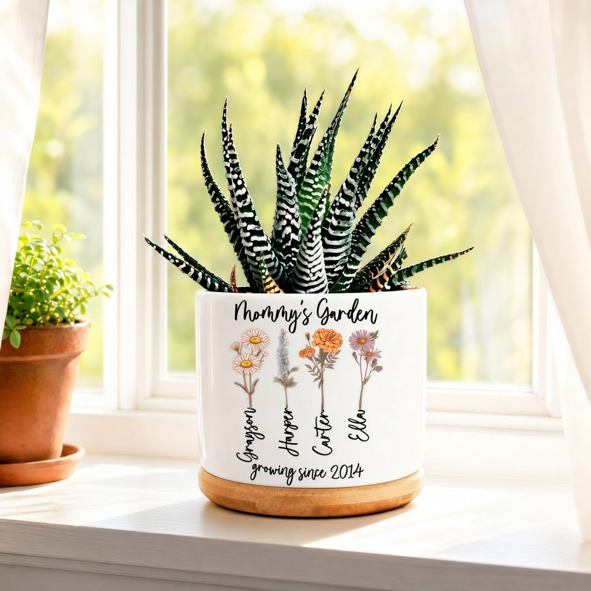 Custom "Mommy's Garden" white ceramic planter with birth flowers and a succulent plant sitting on a windowsill.