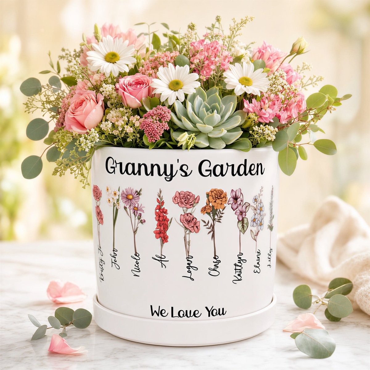 Personalized 'Granny's Garden' birth flower planter featuring custom watercolor flowers and names like Kirsty, John, and Nicole. This white ceramic pot includes the message 'We Love You' and is shown as a vibrant floral centerpiece, perfect for a personalized grandmother gift.