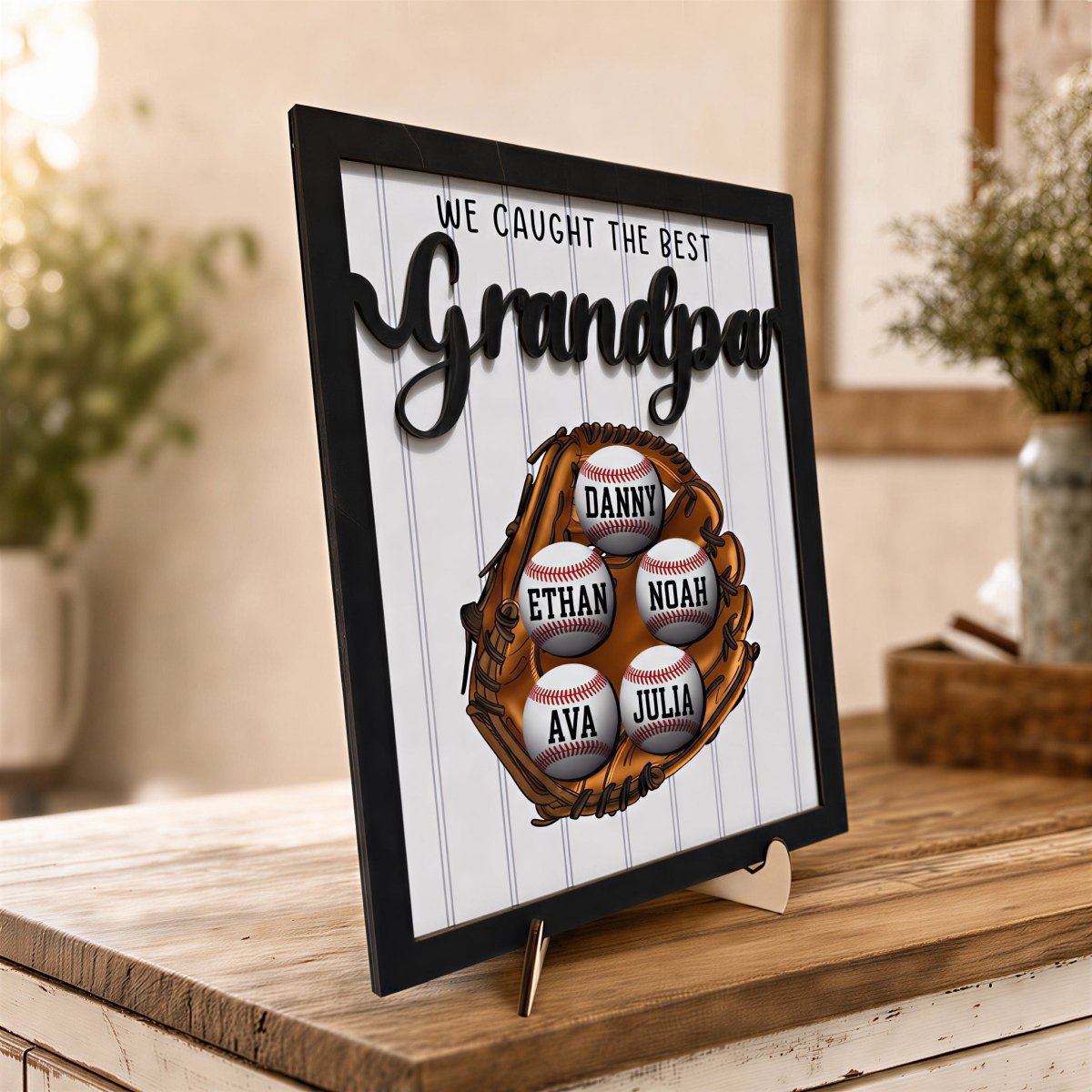 Personalized Grandpa baseball plaque. Custom wooden Father's Day desk sign featuring a 3D baseball glove, rustic black frame, and five customized baseballs displayed on an easel stand.