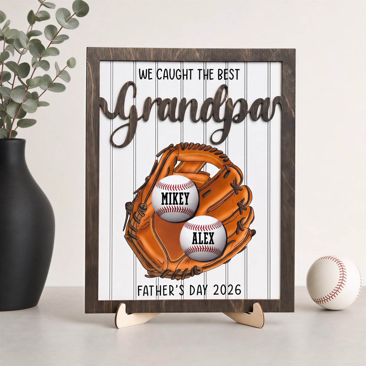 Personalized Father's Day desk plaque for Grandpa. Features a rustic wood frame, 3D raised lettering, and a printed baseball glove holding two custom baseballs with grandkids' names, displayed on an easel.