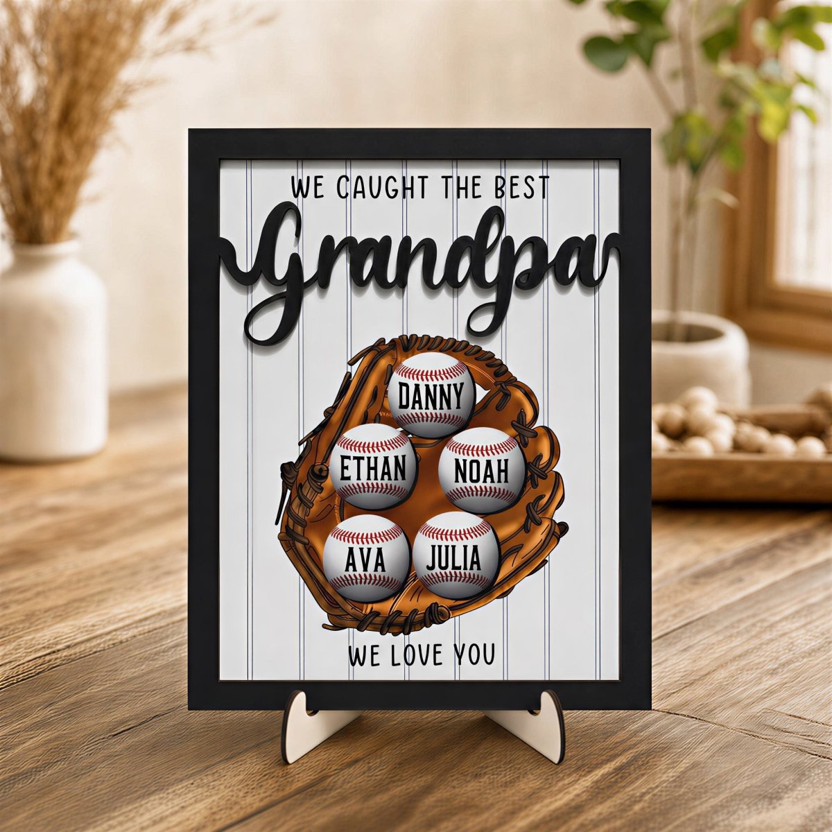 Personalized Grandpa baseball plaque. Custom wooden Father's Day desk sign featuring a 3D baseball glove, rustic black frame, and five customized children's baseballs displayed on an easel stand.