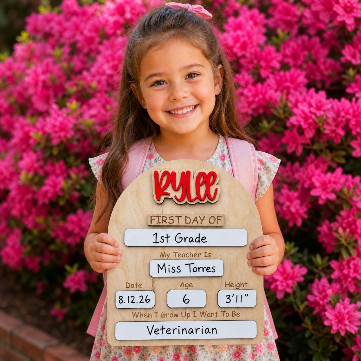 Personalized rounded arch first day of school sign Rylee in red script — girl holding sign with pink azalea flowers